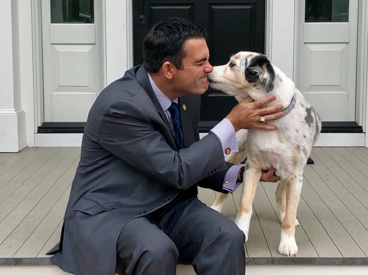 John Bradford kneels on a porch while his dog kisses his nose