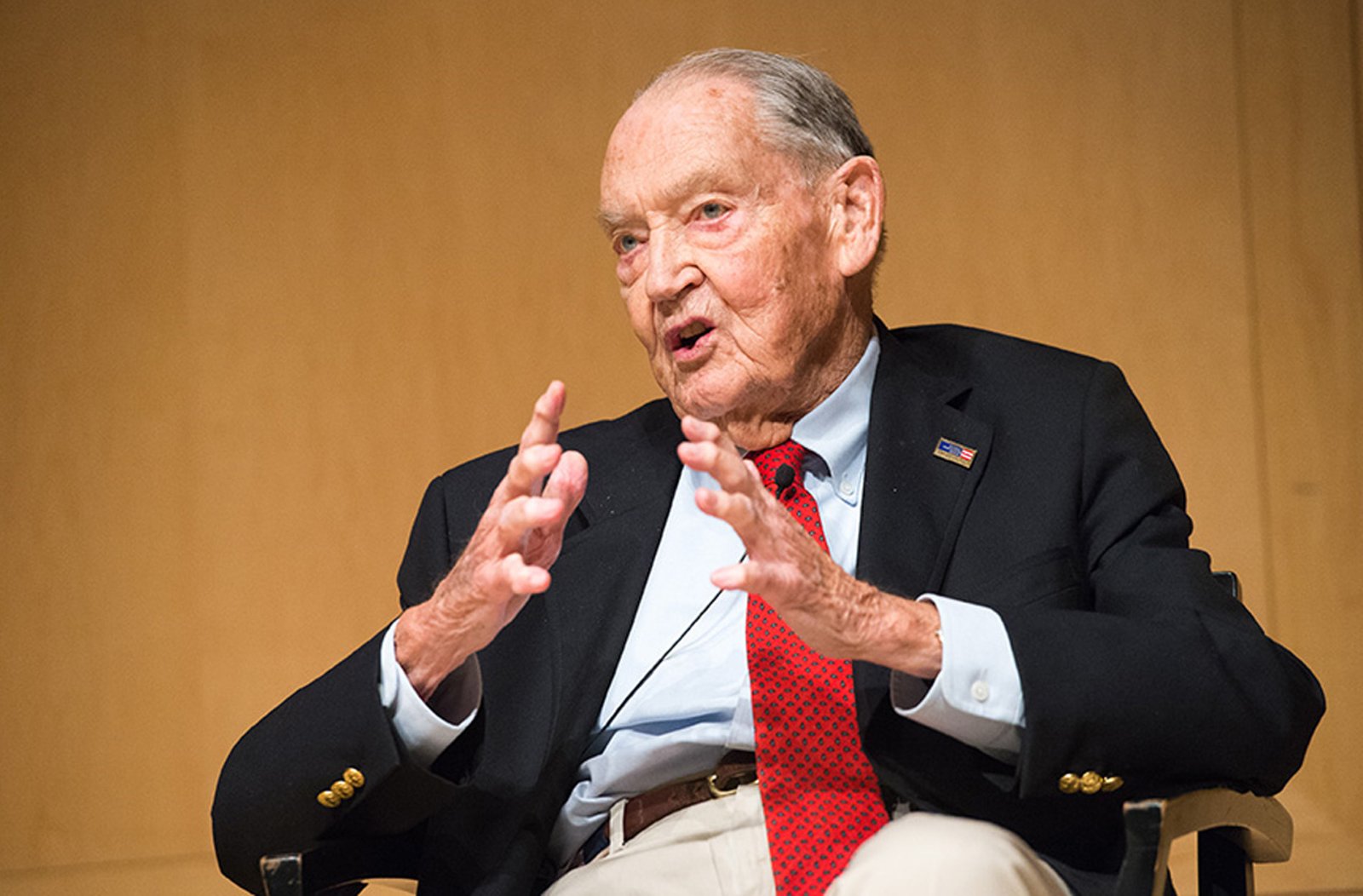 Jack Bogle seated in conversation, gesturing with both hands, wearing a red tie.