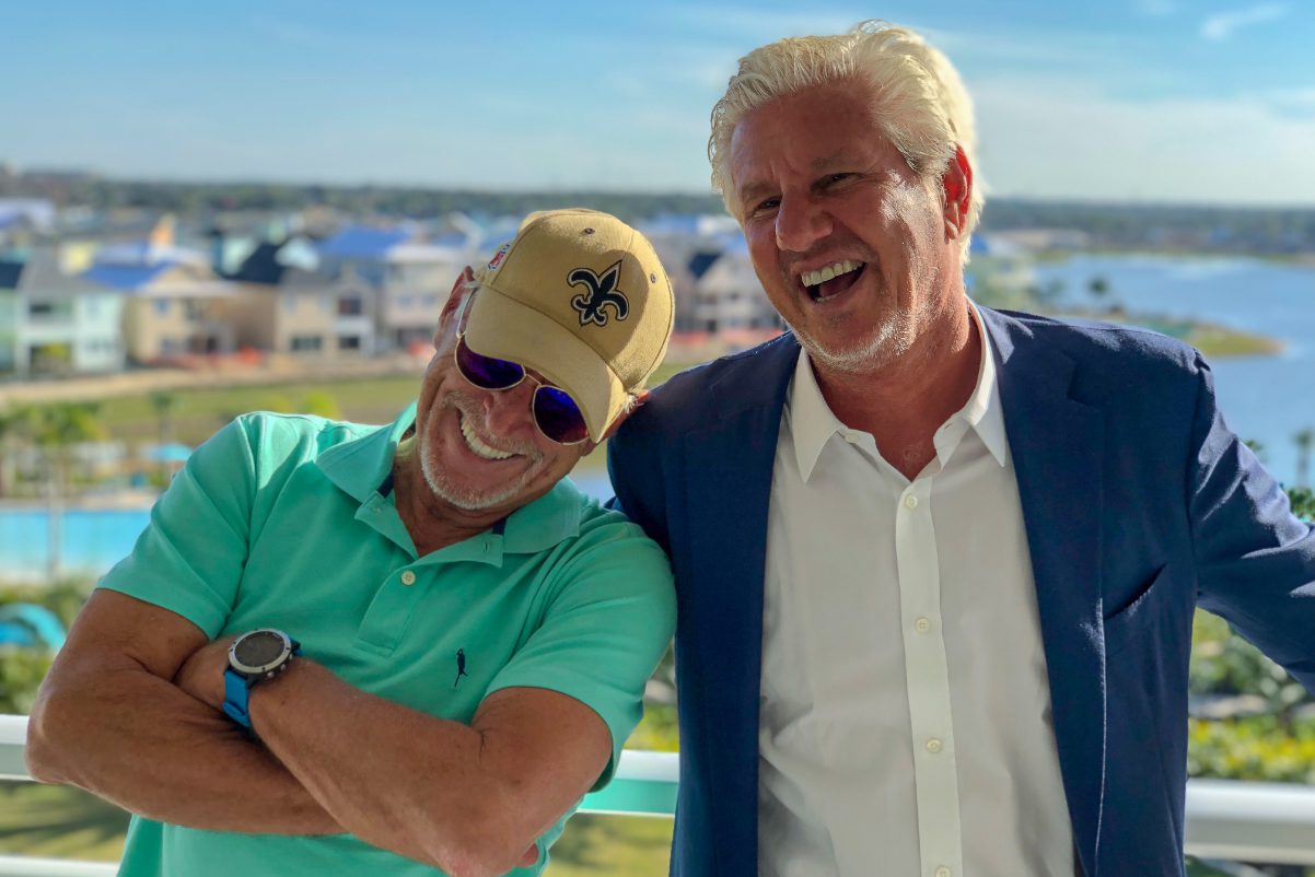 Jimmy Buffett, left, leans against John Cohlan as both smile outdoors beside the water