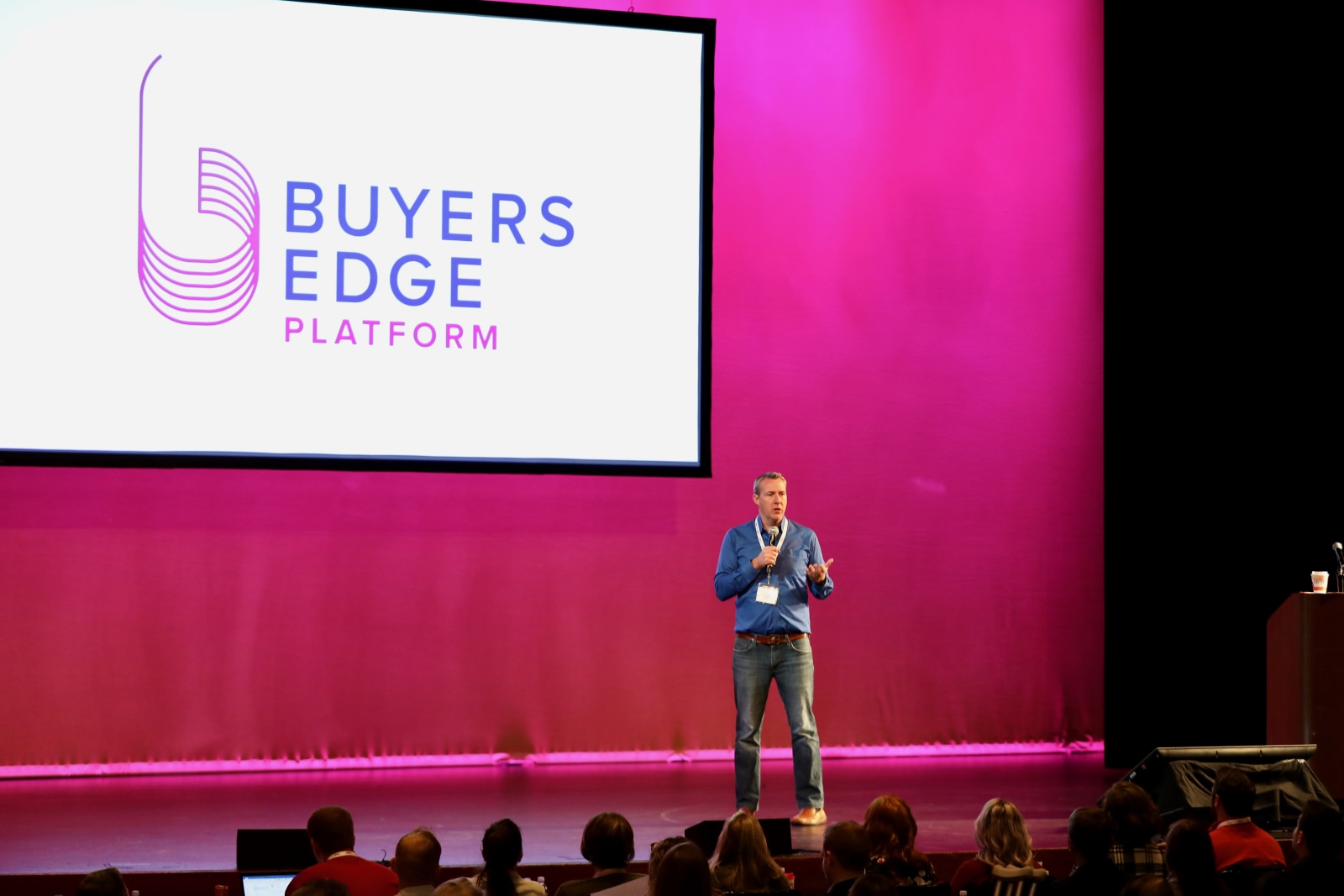 John Davie speaks into a microphone on stage beneath the Buyers Edge Platform name