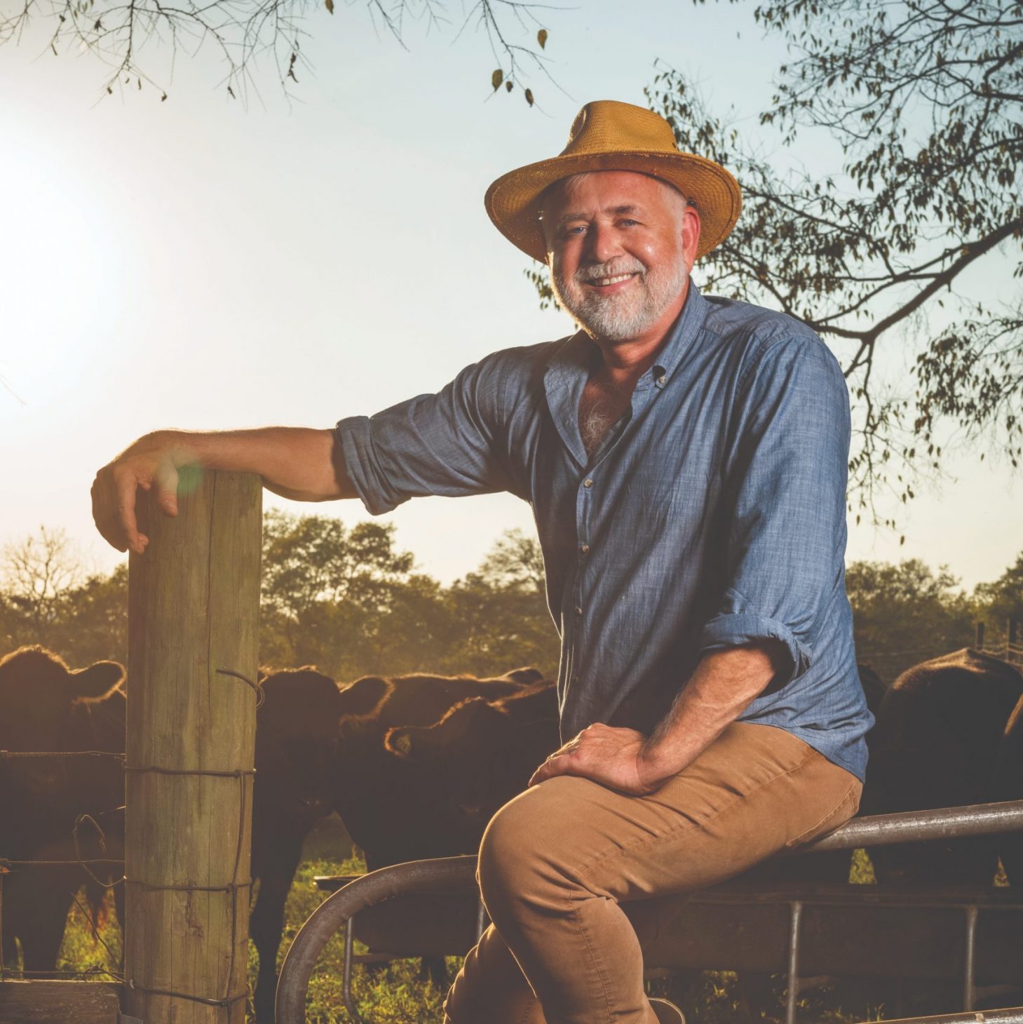 John Dyke in a straw hat, seated on a farm gate at his Lynnville, Tennessee farm