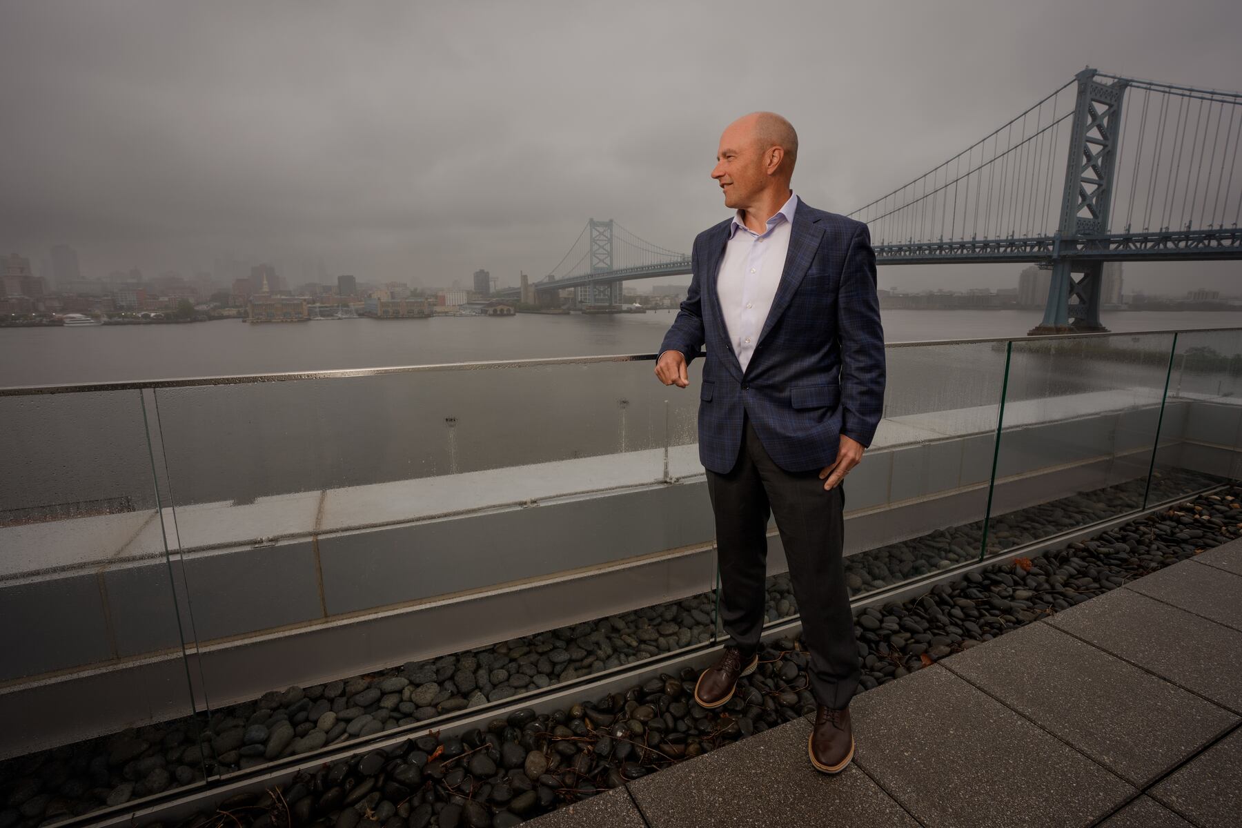 John Griffith standing at American Water’s Camden headquarters, with the Delaware River and Benjamin Franklin Bridge behind him.