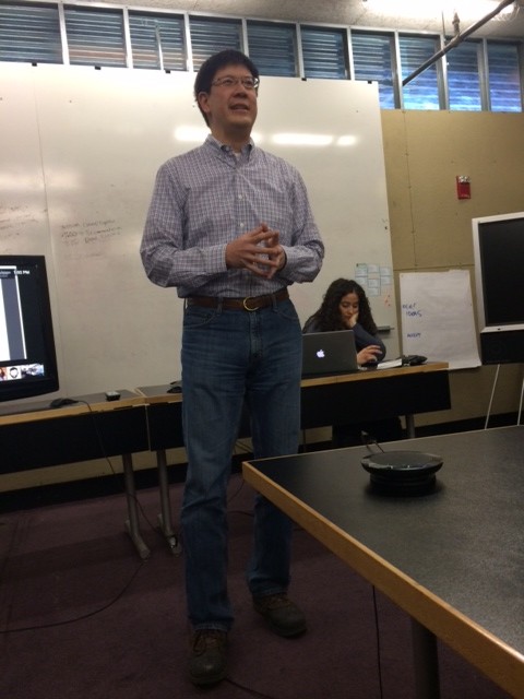 John Chuang standing at the front of a meeting room, speaking with colleagues