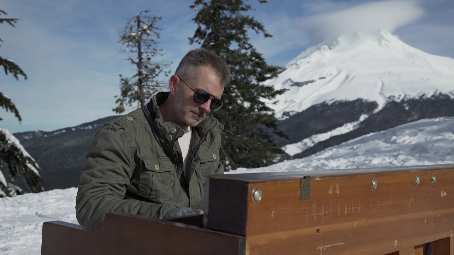 John Horton, performing as Jack Horton, seated at an upright piano in a snowy mountain setting