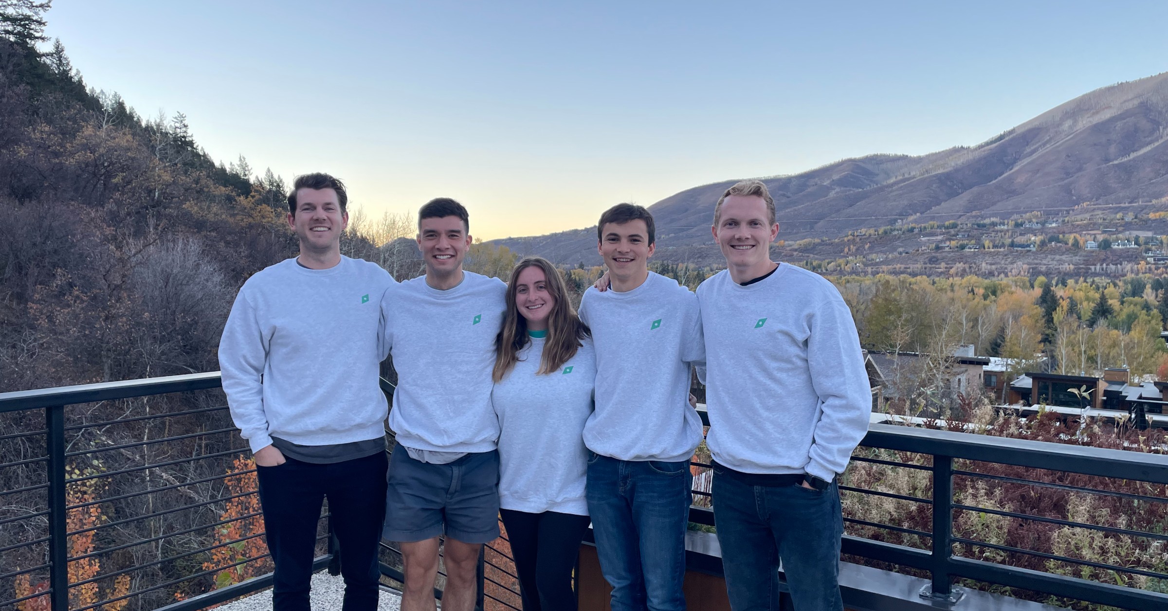 Five early Leland team members standing together outdoors in matching sweatshirts, with John Koelliker at far right