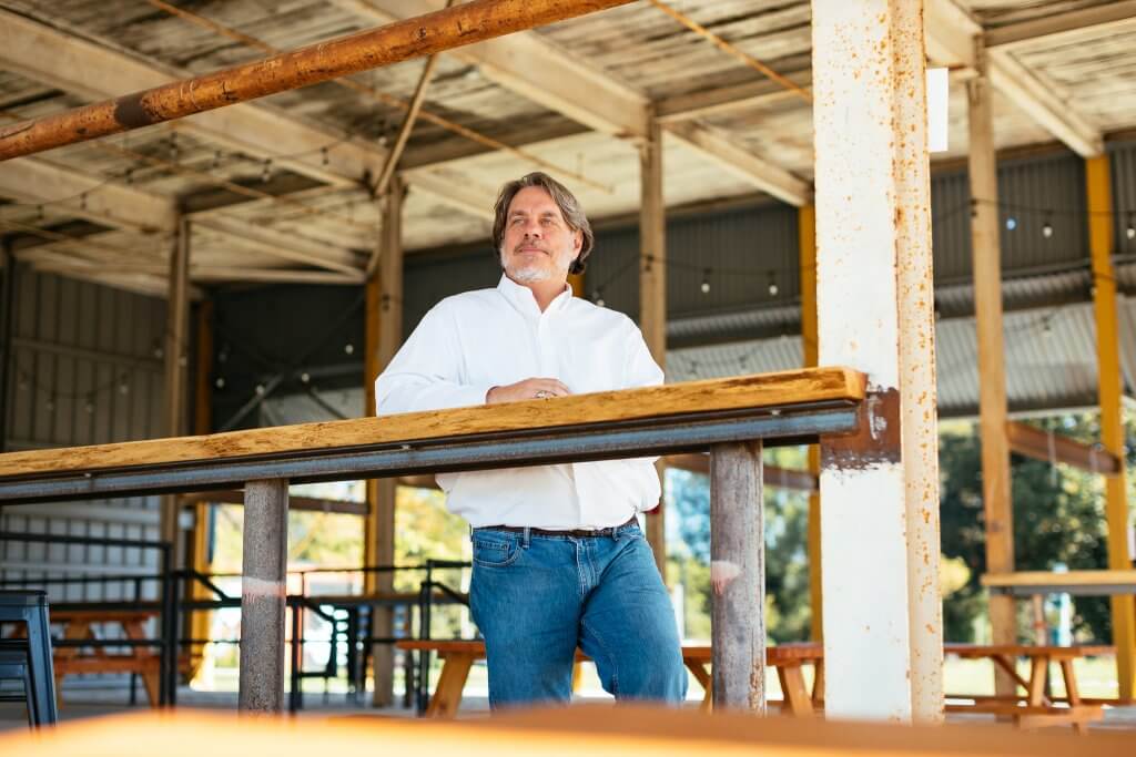 John Moore leaning on a wooden railing in an open industrial interior