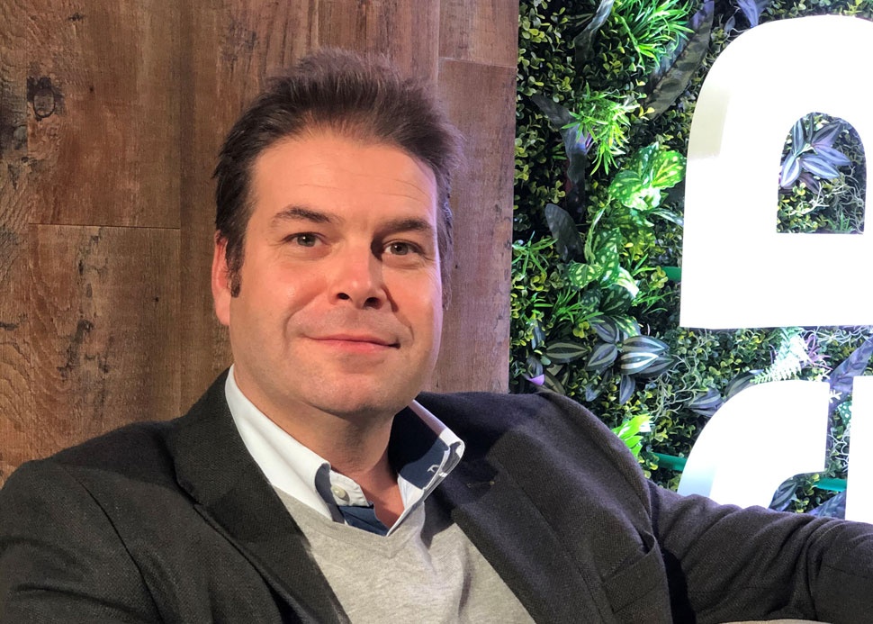 John Natalizia seated beside a wood-panelled wall and greenery