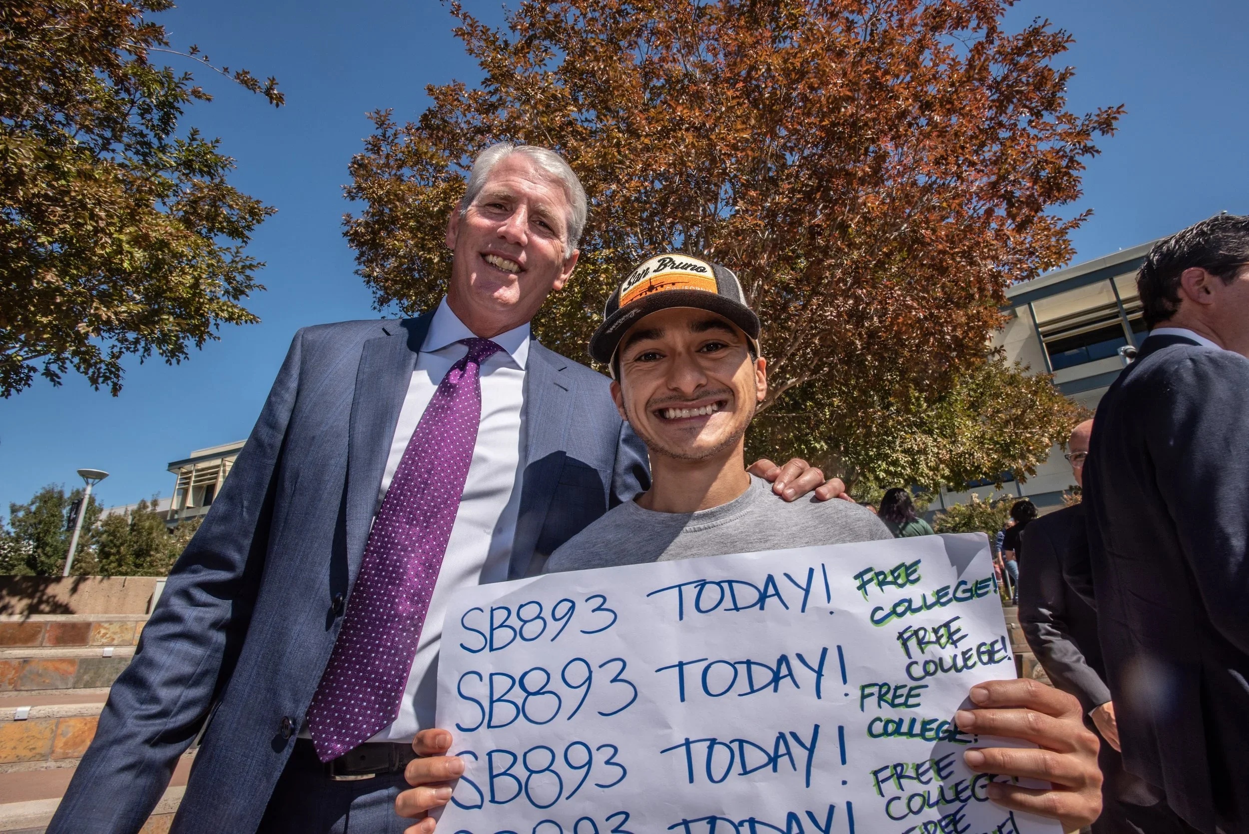John Pimentel standing beside a person holding a handmade SB 893 free-college sign