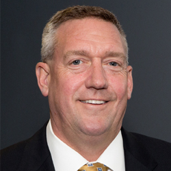 John Priore in a dark jacket and white shirt, in a press portrait published with a 2014 Priority feature