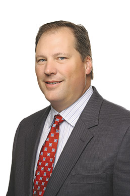 Archival photograph of John Stitz in a dark suit and patterned tie