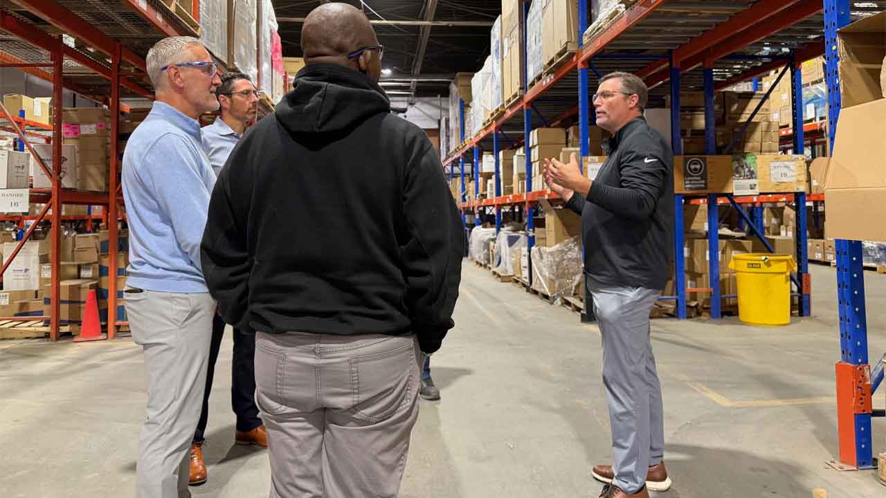John Watwood, at right, talking with colleagues between warehouse racks during a visit with POOLCORP’s Canadian team.