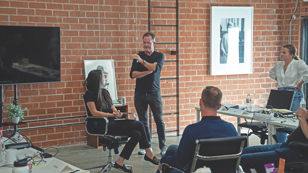 John Wise standing and talking with colleagues around tables in a brick-walled Communify office