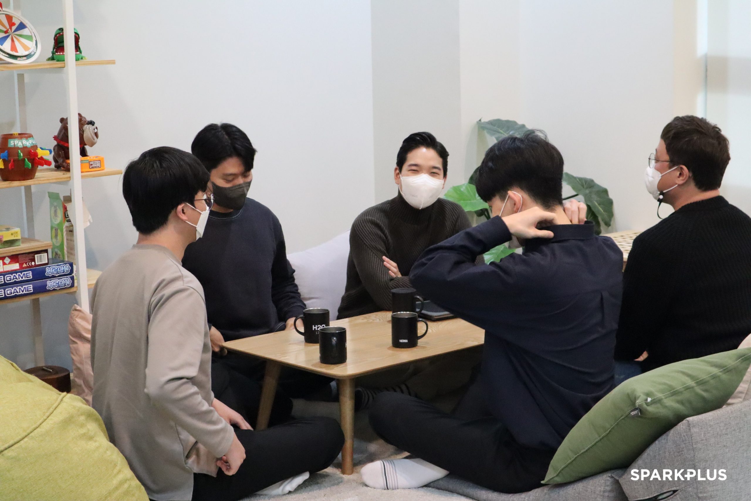 John Lee, seated at the center, in conversation around a table with colleagues at the H2O workspace.