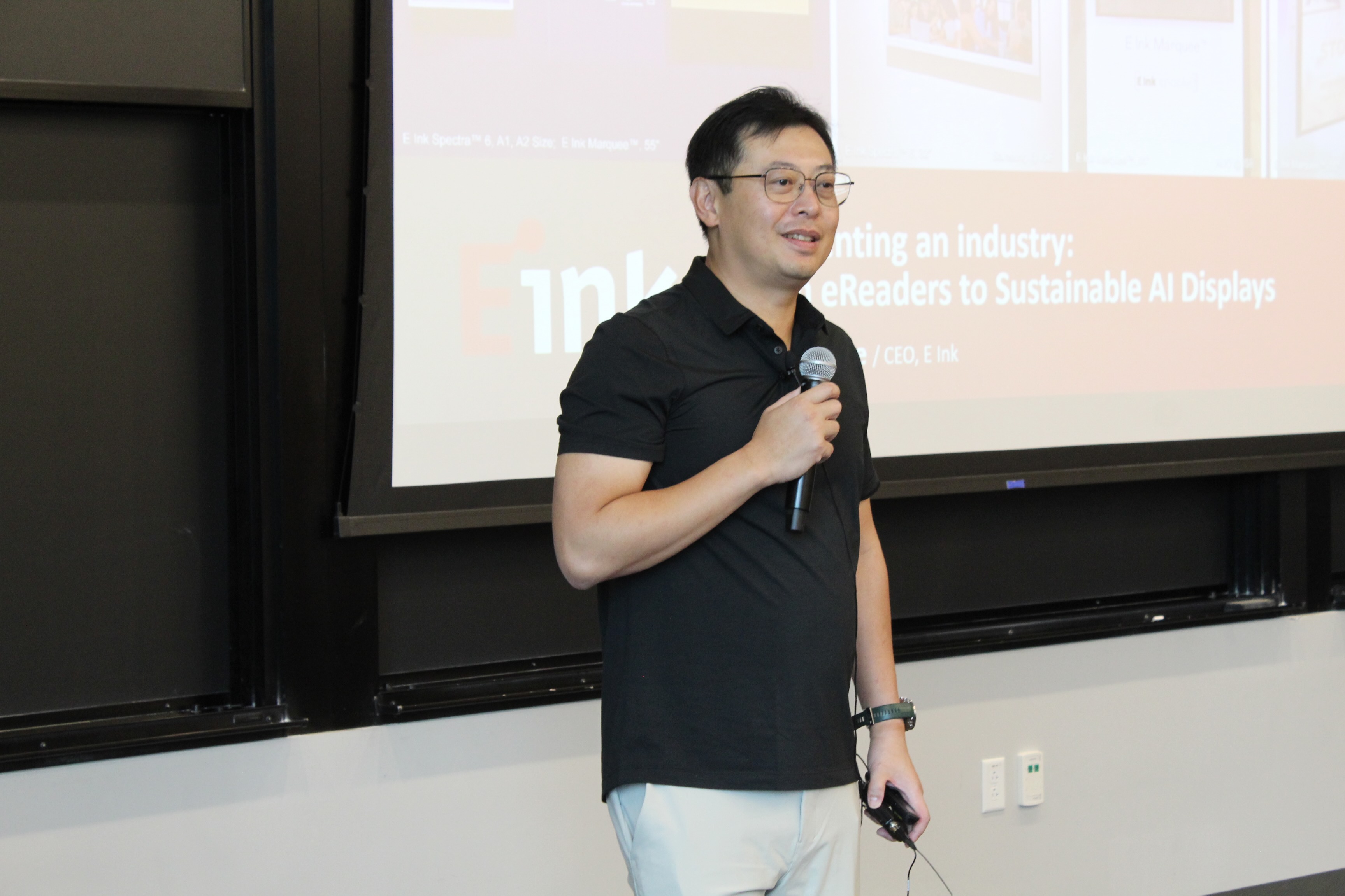 Johnson Lee speaks into a microphone at his Tufts Dean’s Lecture, with his presentation behind him.