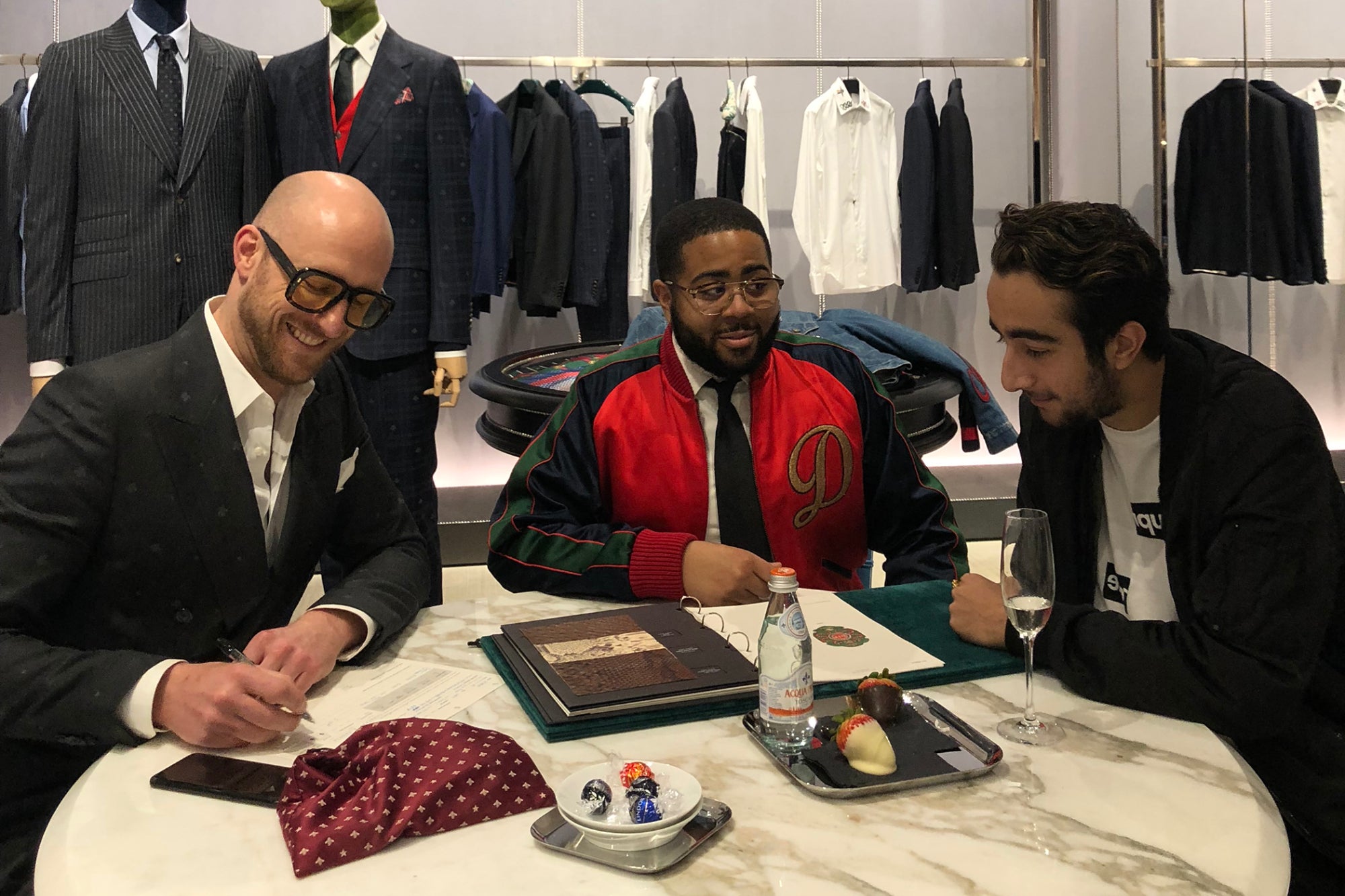 Jonathan Jadali, at right, seated with two other men at a table in a clothing showroom.