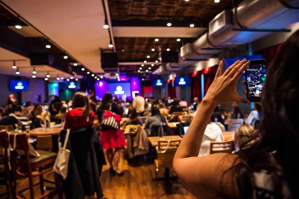 An audience at a Tripleseat gathering, with an attendee photographing the stage