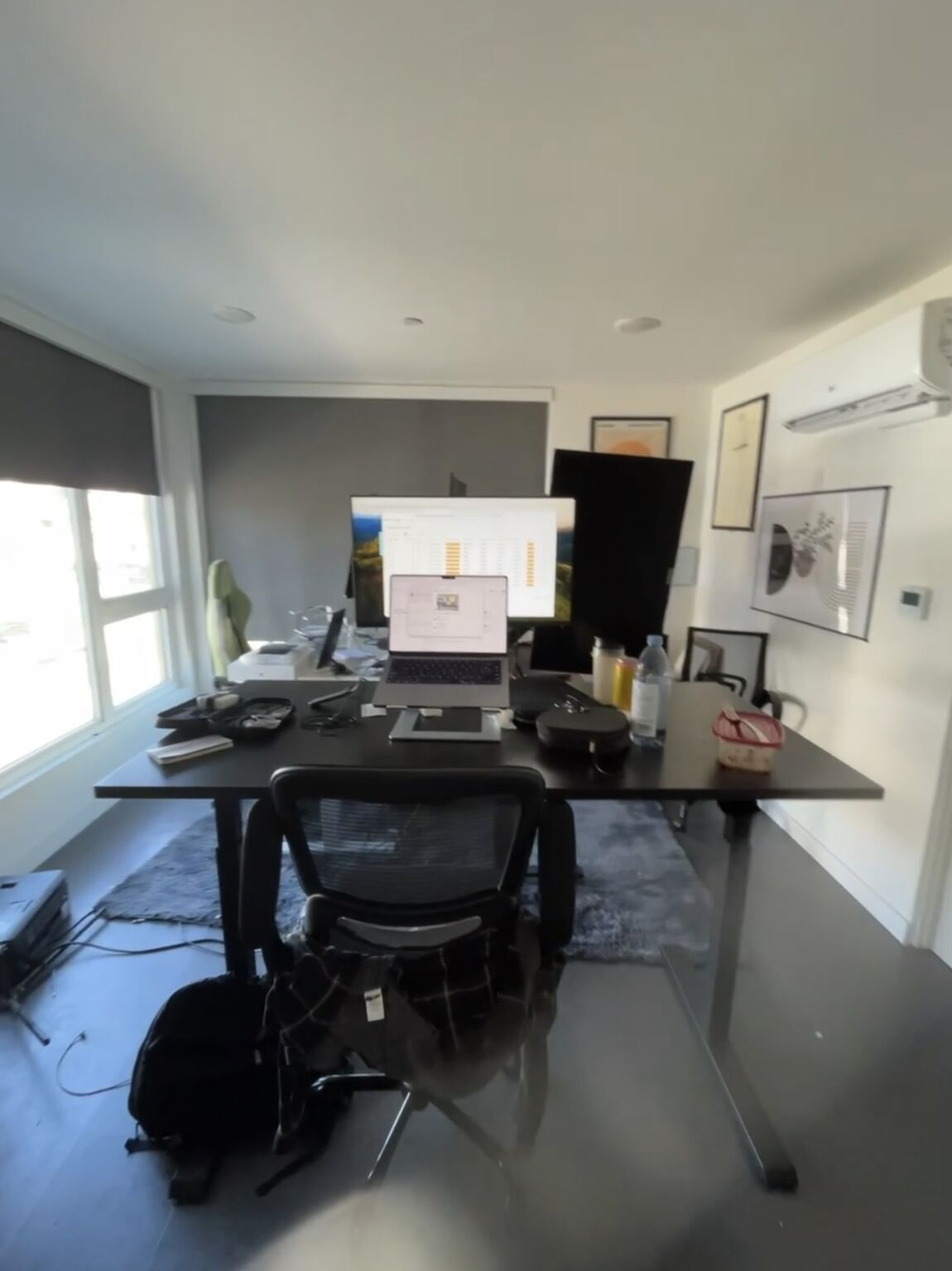 A compact living-room workspace with a laptop, large monitors and office chairs
