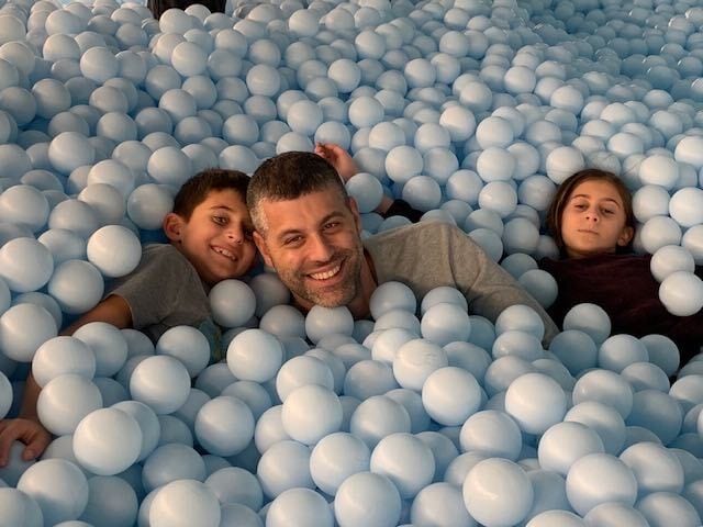 Jonathan Rosen smiling with his two sons in a pool of pale blue play balls