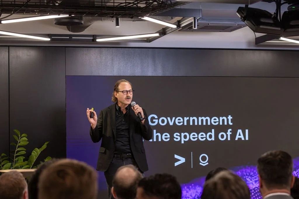 Jonathan Webb speaking into a microphone at an event, with an audience in the foreground