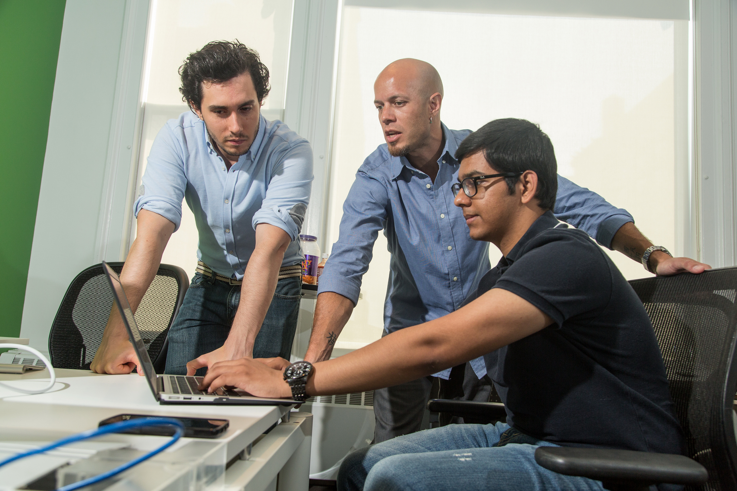 Jonathon Ende leaning over a laptop with colleagues in the SeamlessDocs office