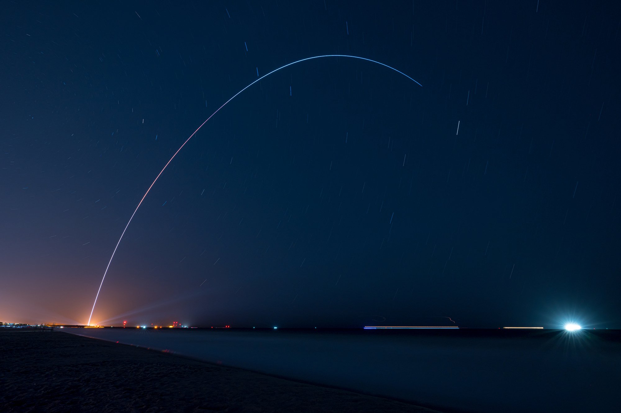 A long exposure of a rocket launch tracing a luminous arc across the night sky