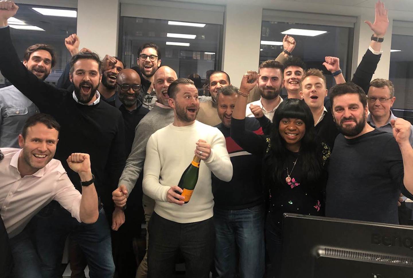 Jos Evans holding a champagne bottle with the AiX team celebrating around him