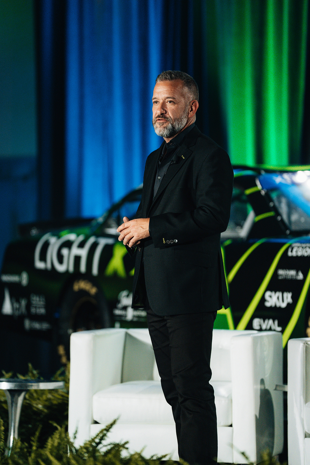 Joseph Anderson speaking at LightX with a branded race car behind him.