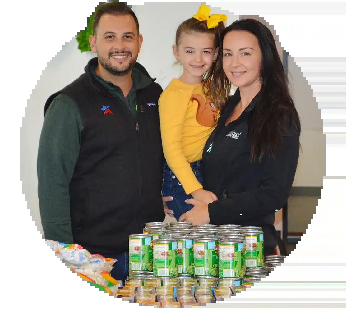 Joseph Camberato and two companions standing behind a table of donated canned food