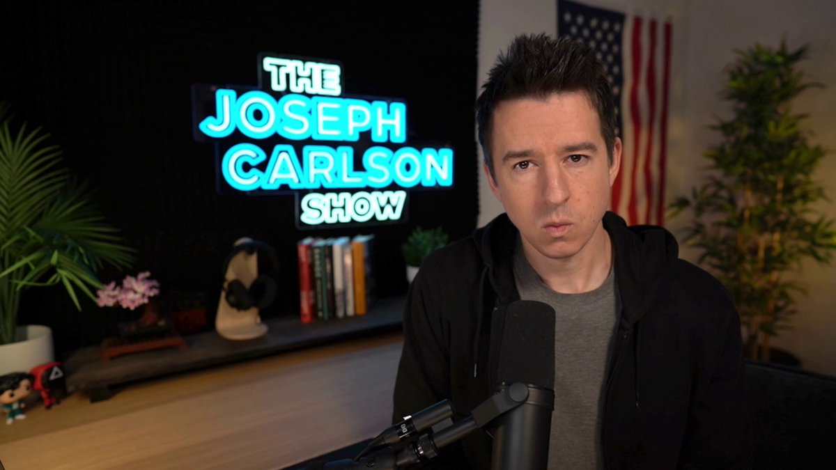 Joseph Carlson recording The Joseph Carlson Show in his studio, with a microphone and illuminated show sign