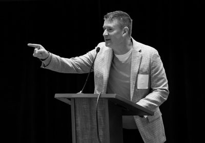 Joseph King speaking at a lectern and gesturing toward the audience
