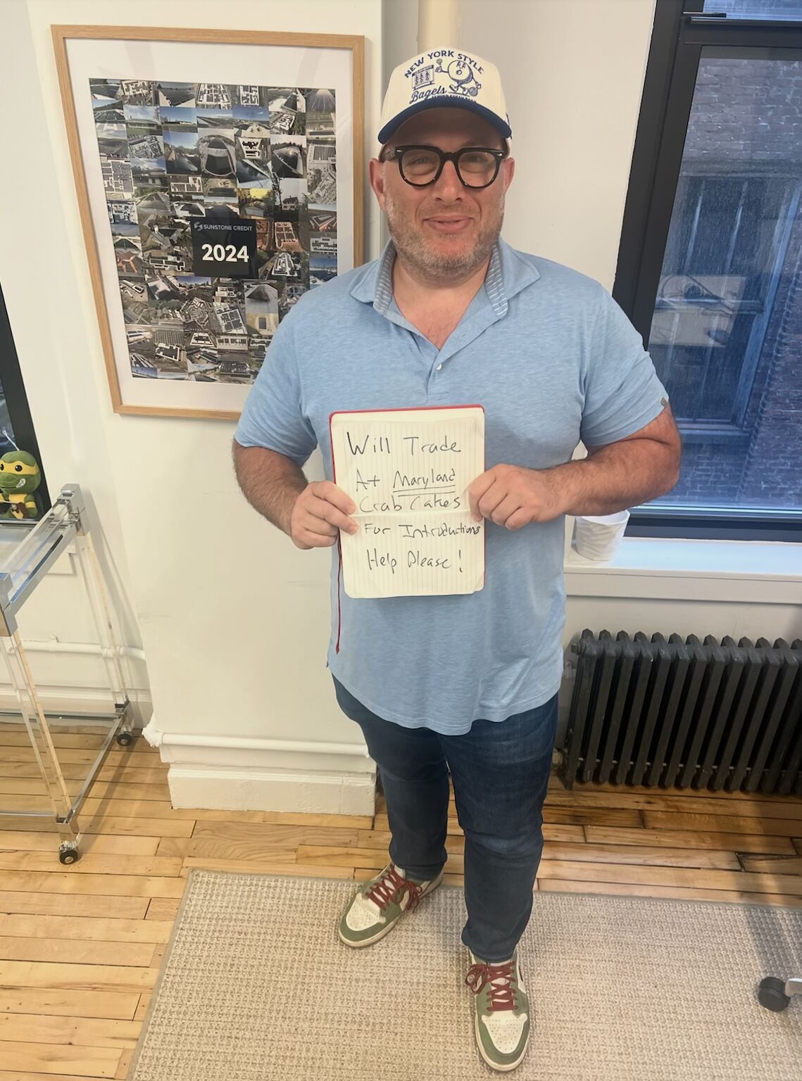 Josh Goldberg in a bagel-themed cap holding a sign offering Maryland crab cakes for introductions