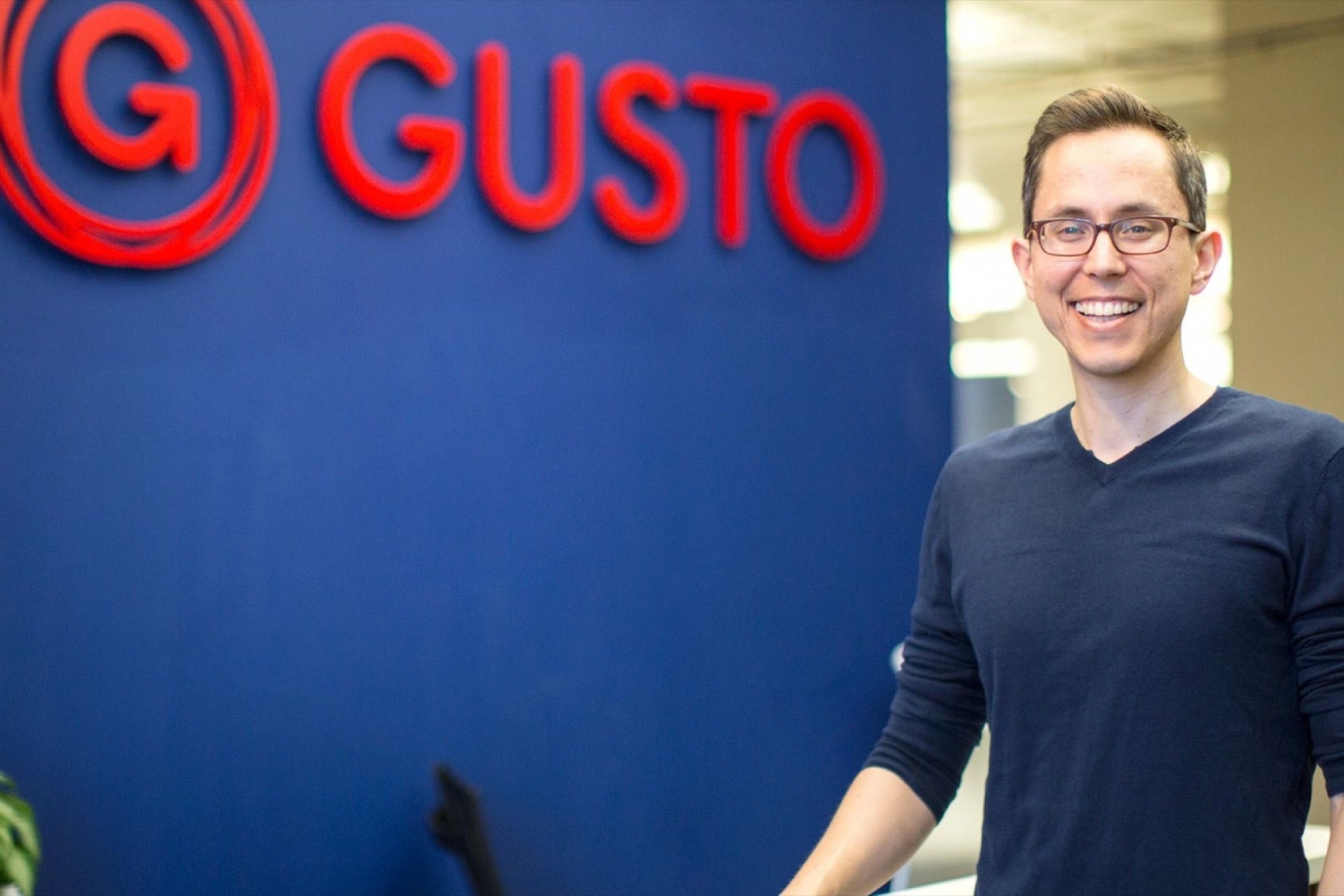 Josh Reeves standing beside the Gusto sign in the company’s office