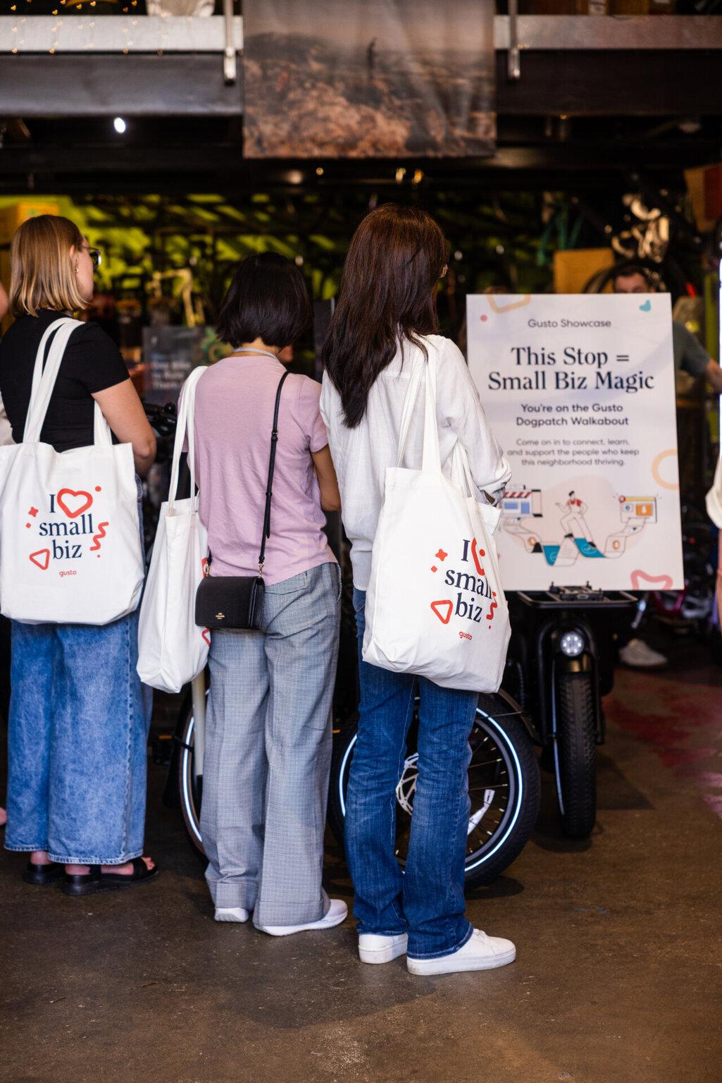 Gusto Showcase attendees carrying small-business tote bags during a Dogpatch neighborhood walkabout