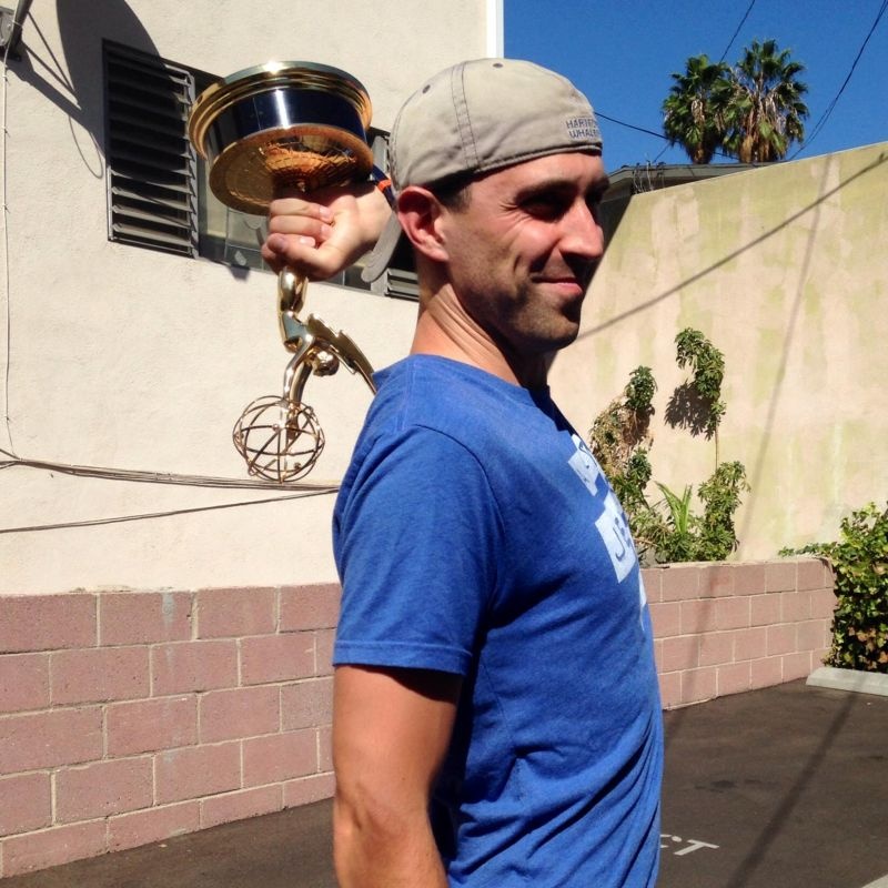 Josh Schachter holding an Emmy behind his shoulder outdoors