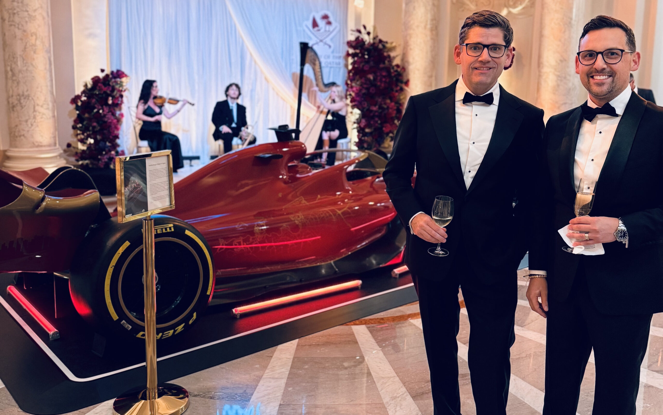 NJI co-founders Josh Shultz and Nathan Imperiale in tuxedos beside a red racing-car display