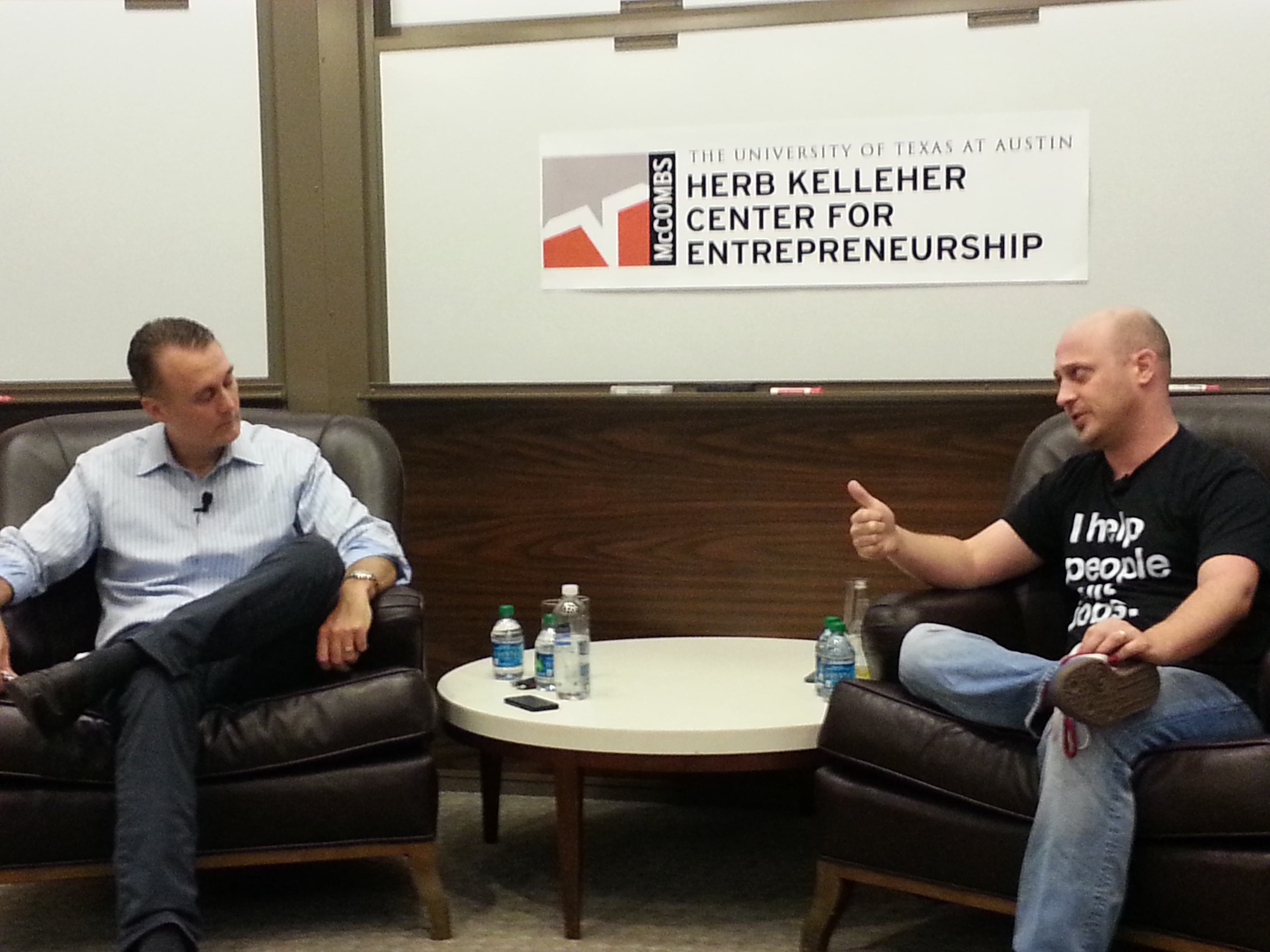 Brett Hurt seated on the left, interviewing Joshua Baer in an I help people quit jobs T-shirt at UT Austin