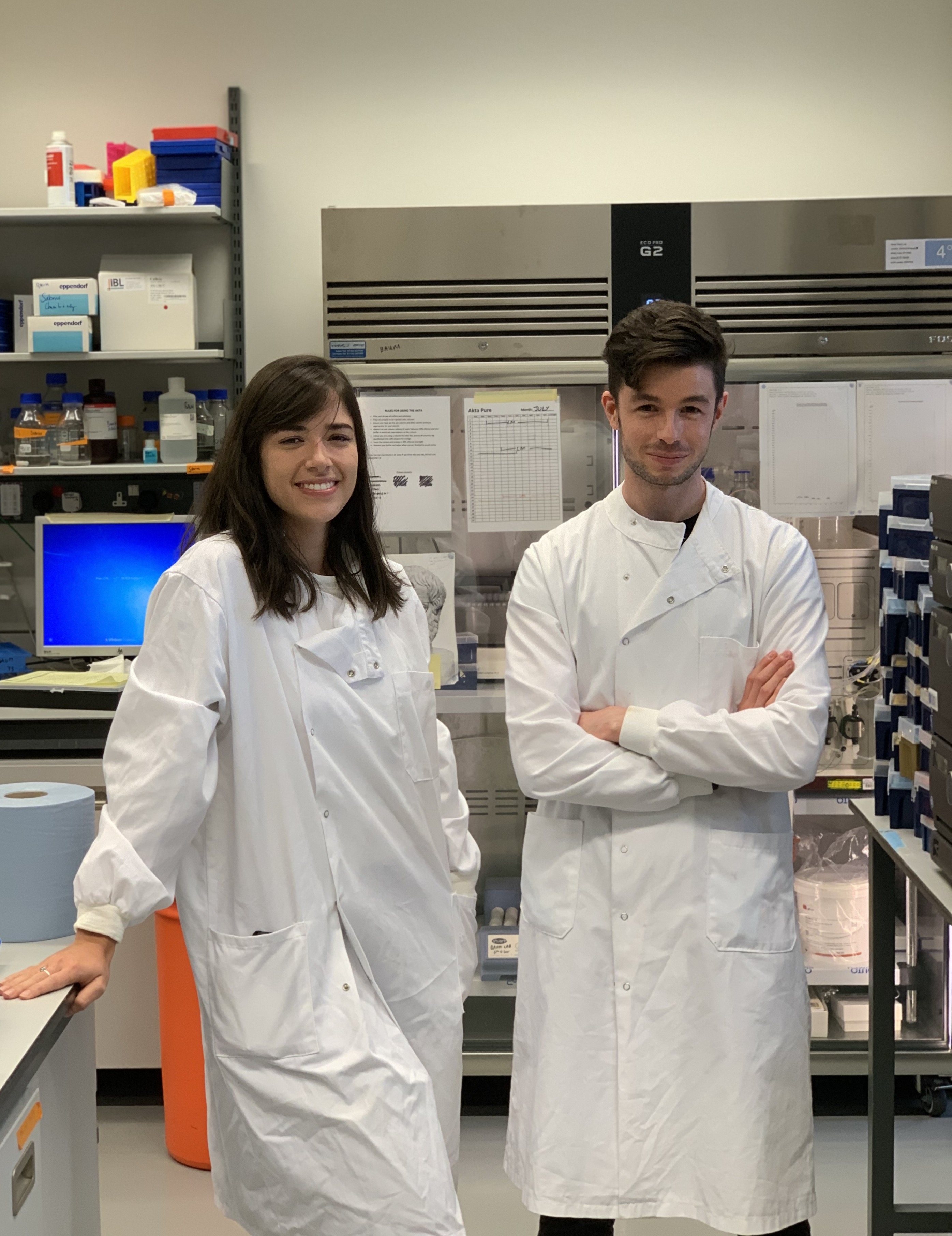 Ariane Gomes, left, and Joshua Blight, right, standing in a laboratory