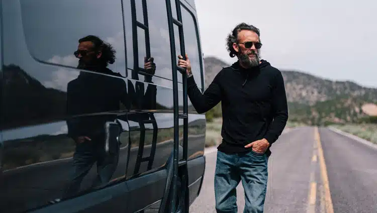 Joshua Waldron beside a black van on a mountain road