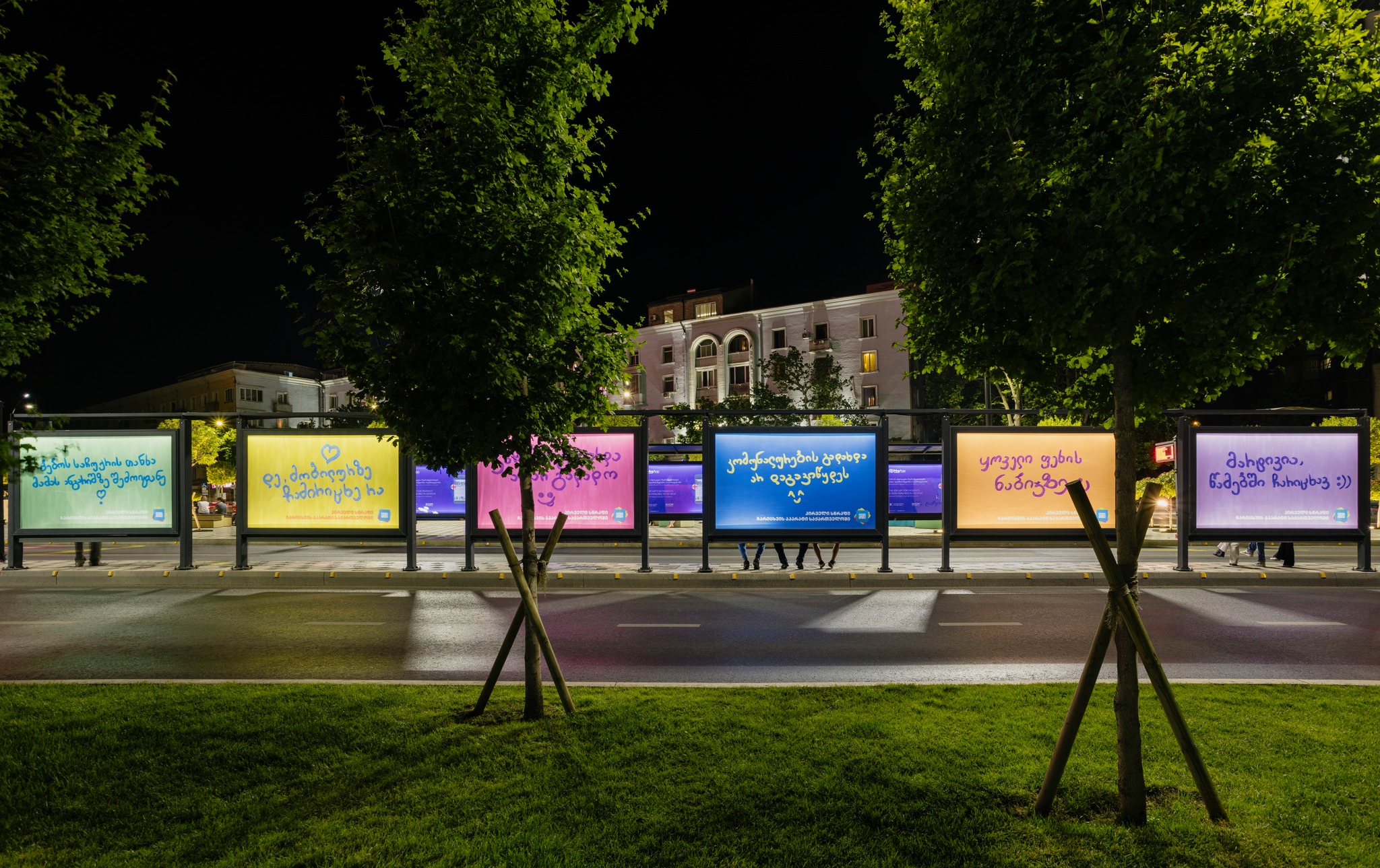 A row of colorful PayBox advertising panels beside a street at night