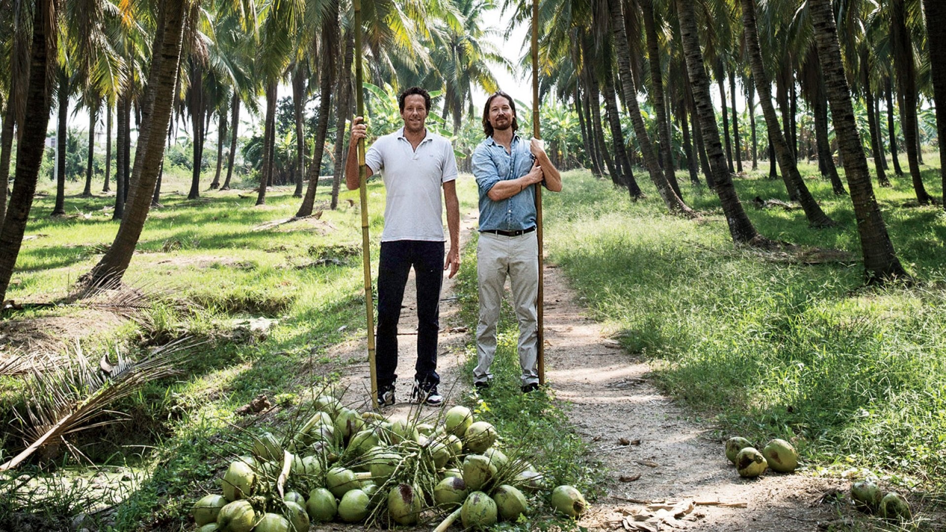 Douglas Riboud, left, and Justin Guilbert holding harvesting poles in a coconut grove in Thailand