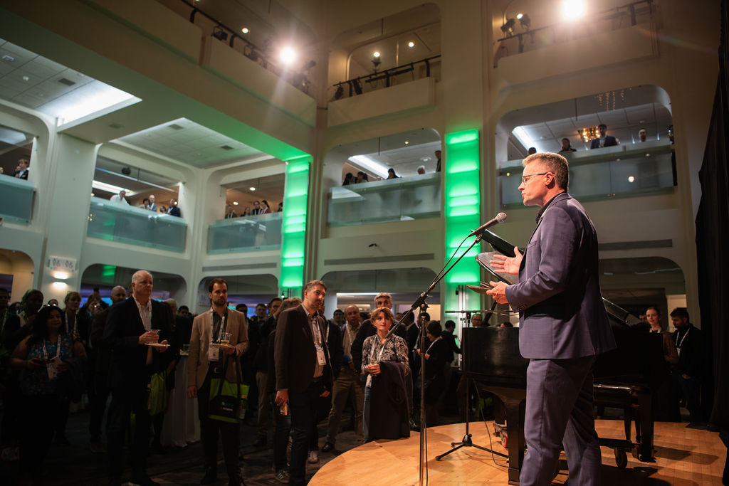 Justin Riemer speaking at a microphone to a gathered audience