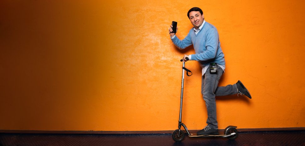 ParkHub founder George Baker posing with a scooter and handheld device against an orange wall