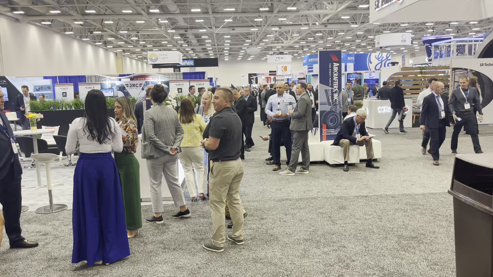 Visitors talking among aviation exhibits, with seating and overhead company signs