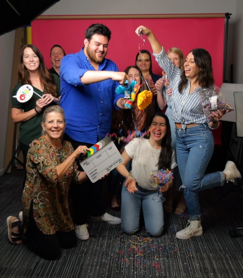 K Harvey Brand Partners team members gathered playfully around a production clapperboard