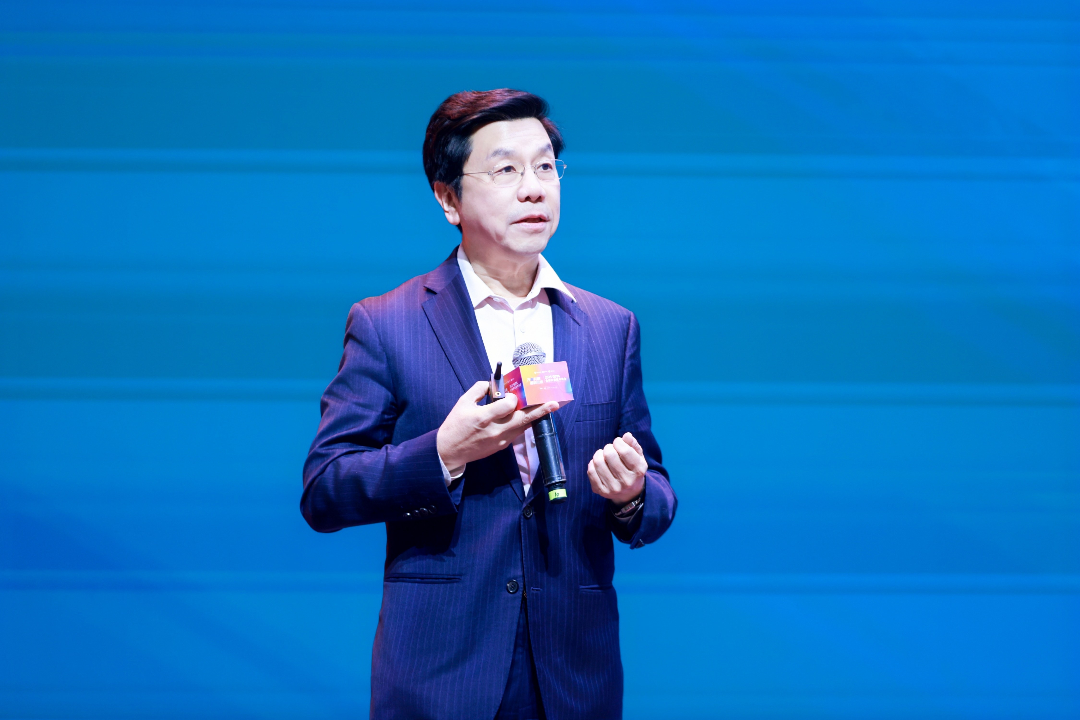 Kai-Fu Lee speaking on stage with a microphone against a blue backdrop