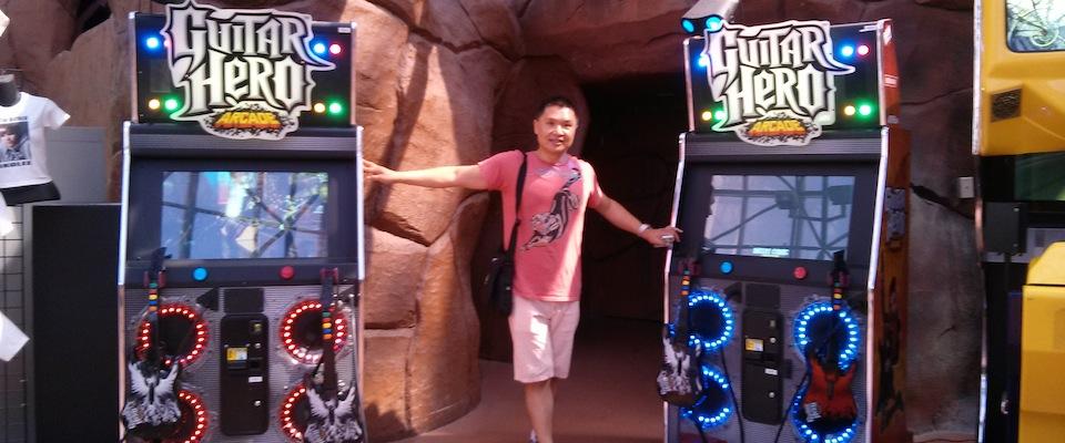 Kai Huang standing between two Guitar Hero arcade cabinets