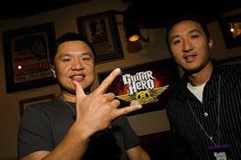 Charles and Kai Huang photographed together with Guitar Hero Aerosmith artwork behind them
