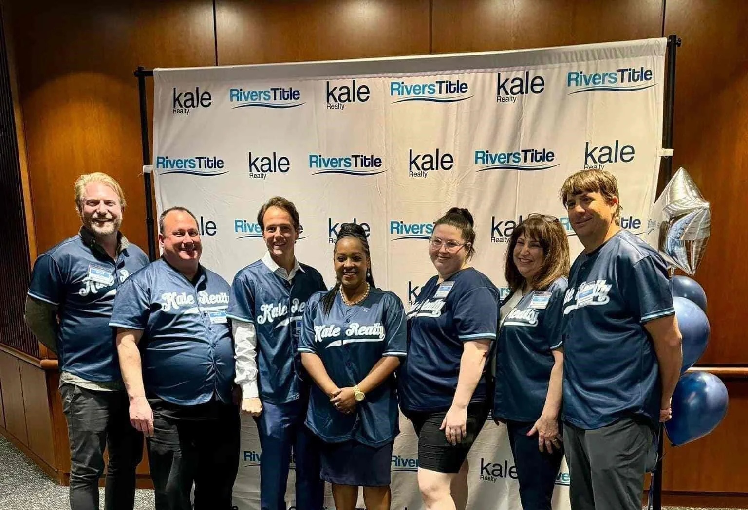 Seven people wearing Kale Realty shirts at a company event