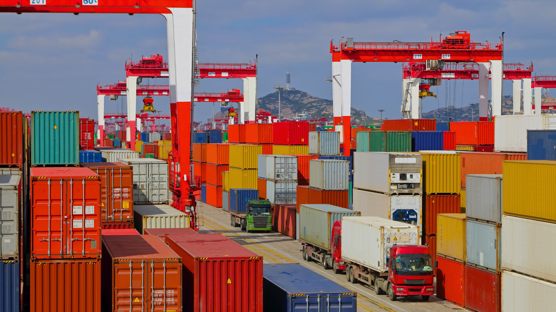A busy container terminal with red gantry cranes, stacked containers and trucks