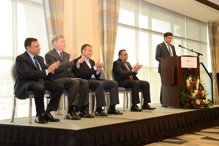 Kalyan Kodali speaking at a lectern in Erie as company and local leaders applaud